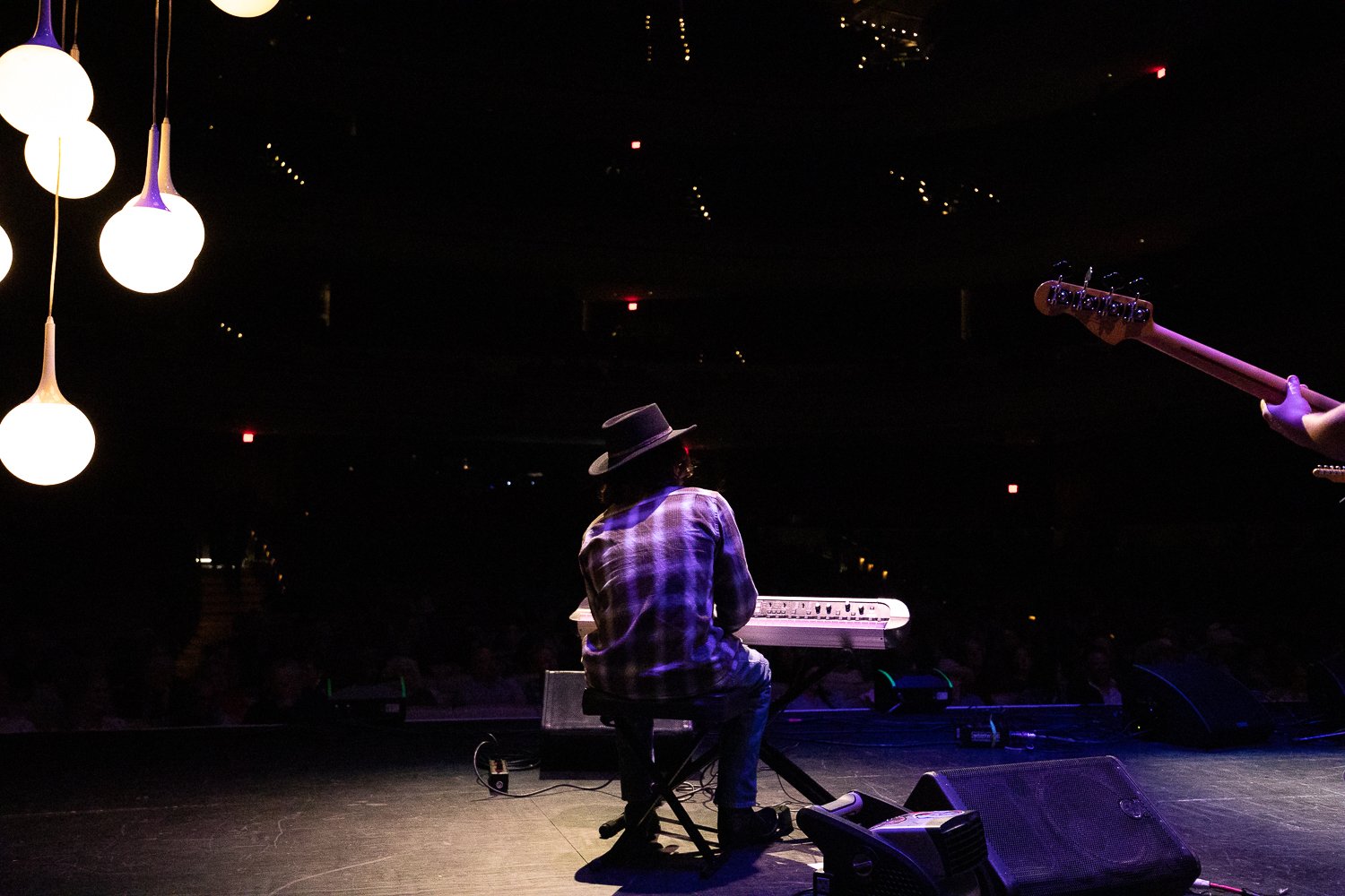 Finn Dickens at the keys from behind, facing the crowd under hanging bulb lights
