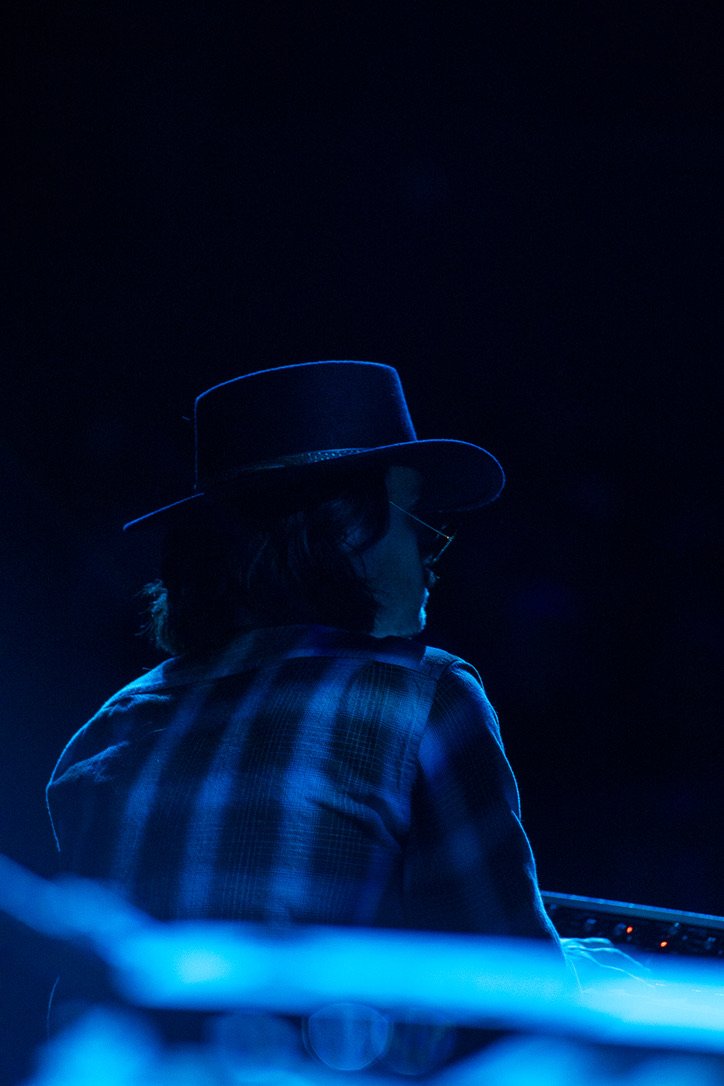 Finn Dickens seen from behind in blue stage light, wearing a wide-brim hat