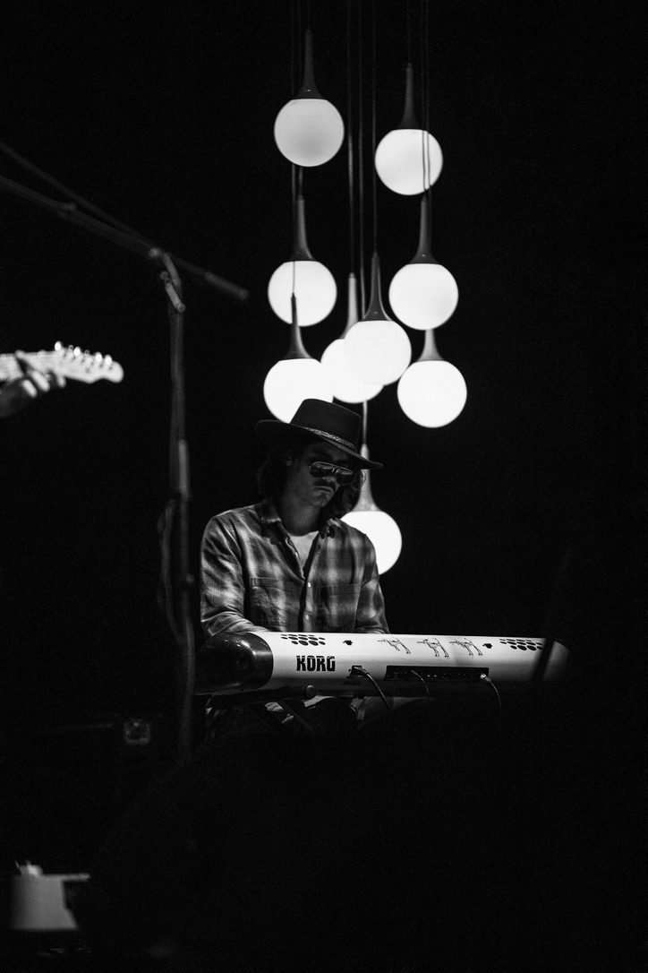 Finn Dickens at the keys beneath a cluster of hanging bulb lights