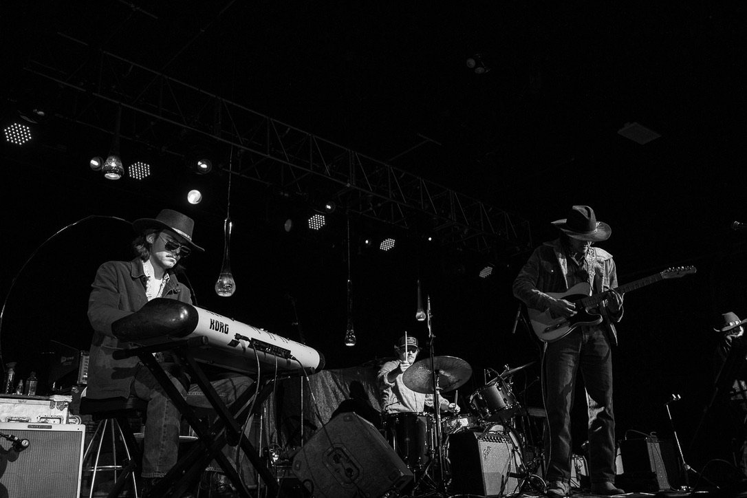 Finn Dickens on keys with the full band on stage under hanging bulb lights