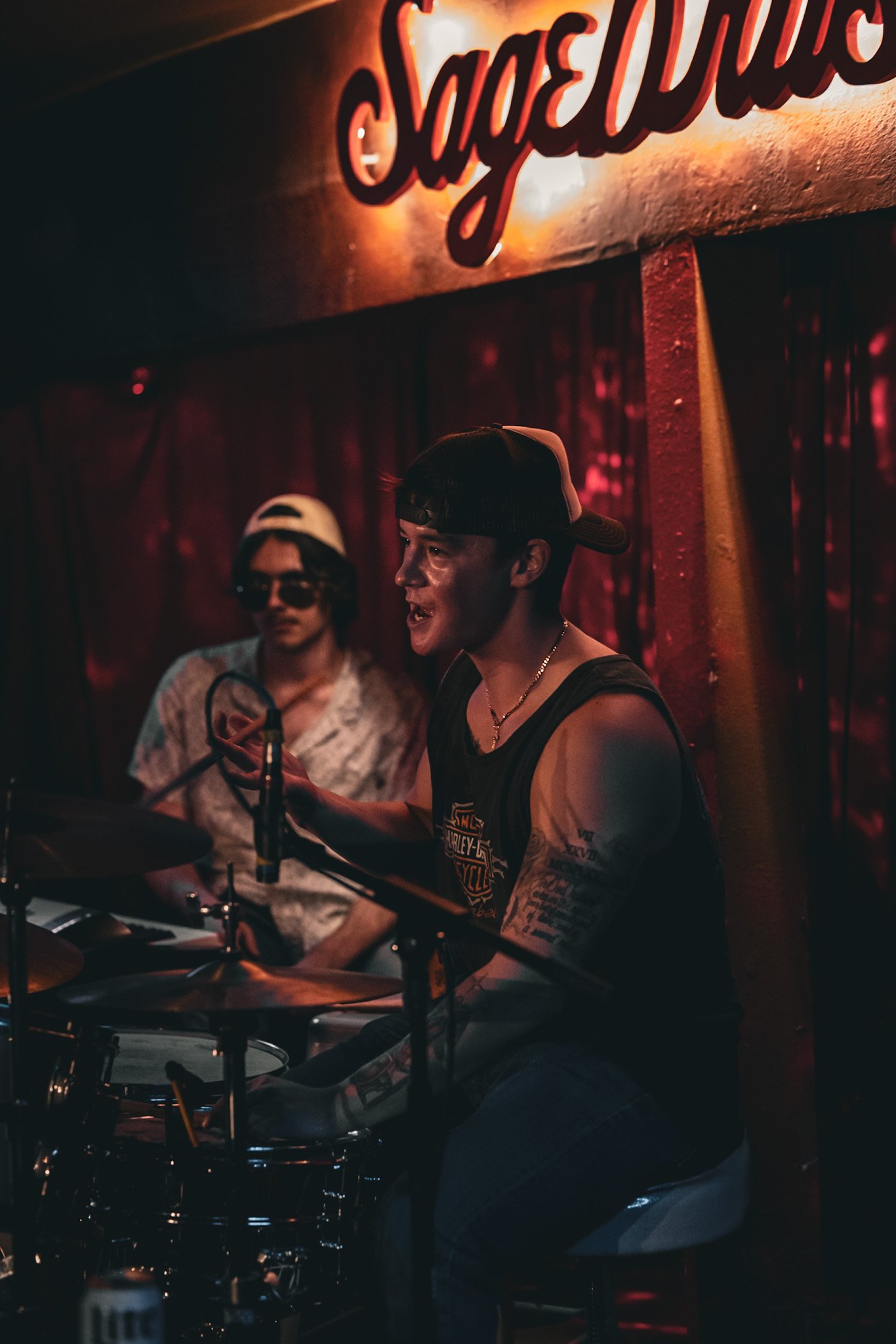Drummer and bandmate lit red under the Sagebrush sign